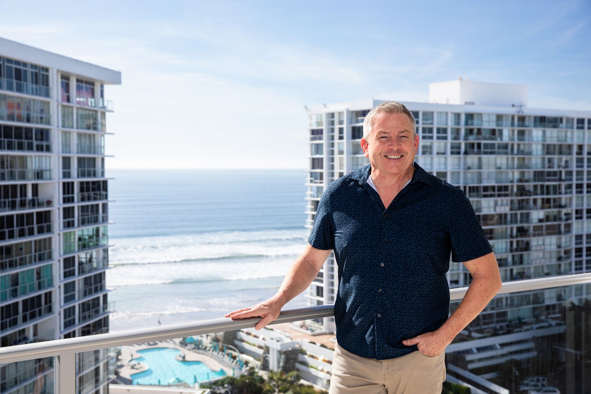Tom Tilford standing on a balcony with the Coronado Shores towers and ocean behind him